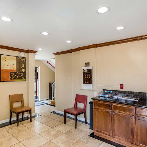 The image shows a small waiting area with two chairs, a counter, a painting, and tiled flooring. There's a hallway leading to another part of the building.