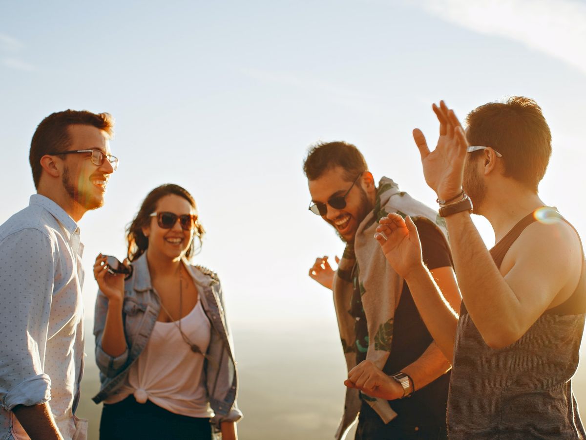 Four people are outdoors, smiling and dancing in the sunlight. They seem to be enjoying themselves and having a good time together.