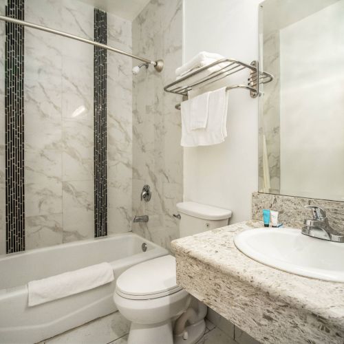 A bathroom with marble walls, a bathtub, a toilet, a sink with a large mirror, and a towel rack above the toilet.