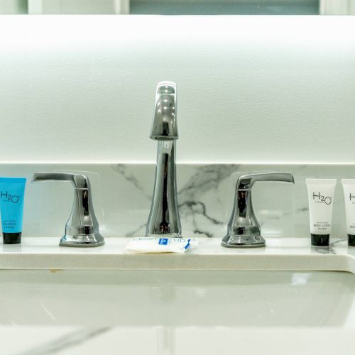 A bathroom sink with a marble backsplash, chrome faucet, and four tubes of H2O+ products, plus a soap packet on the countertop.