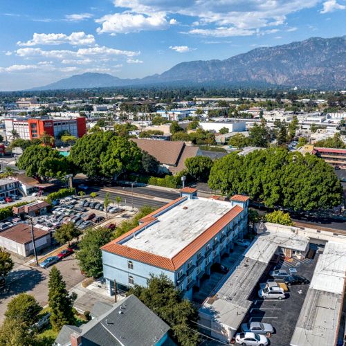 An aerial view of a suburban area with buildings, trees, and mountains in the background on a clear day.