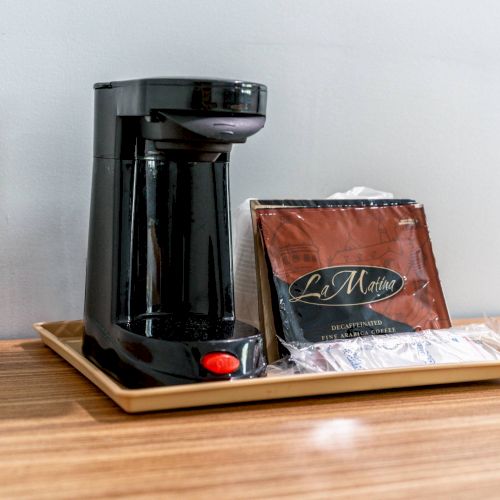 A coffee maker with a tray, coffee packet, and accessories placed on a wooden surface.