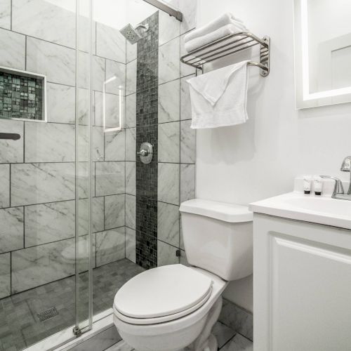 The image shows a modern bathroom with a glass shower, toilet, and sink with toiletries on the counter, all featuring a sleek design.