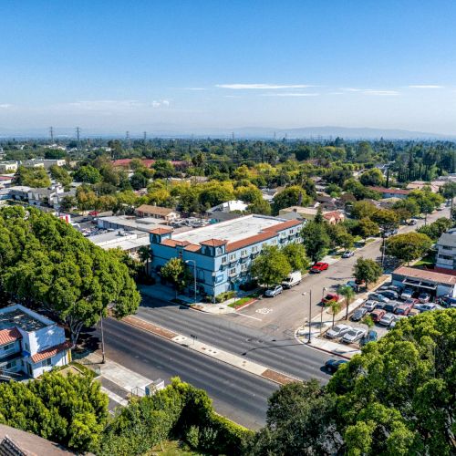 Aerial view of a suburban area with tree-lined streets, buildings, and houses under a clear blue sky.