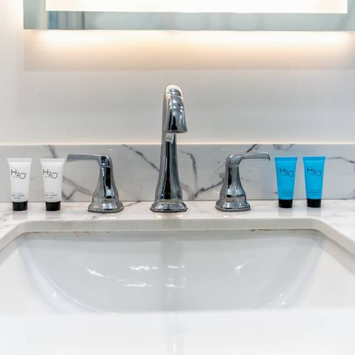 A marble sink with a modern faucet and four toiletries, two white tubes and two blue tubes, neatly arranged on the countertop.