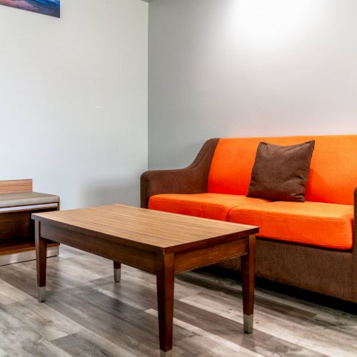 The image shows a room with a brown and orange sofa, a wooden coffee table, and a small side bench, set on a light wood floor.