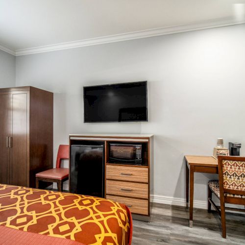 The image shows a hotel room with a bed, TV, wardrobe, mini fridge, desk, chair, and wooden floor, exuding a modern and cozy atmosphere.