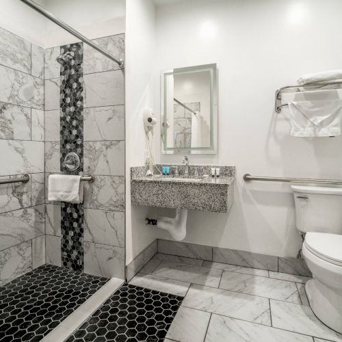 A modern bathroom with a walk-in shower, sink, and toilet. Marble tiles and a wall-mounted towel rack are visible. The setting is elegant.