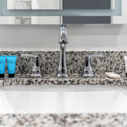 A bathroom sink with a granite countertop, a modern faucet, and various toiletries including blue and white tubes arranged on either side.