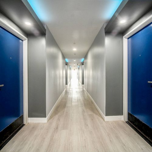 A brightly lit hallway with blue doors on both sides and a light wood floor, creating a modern, sleek design.