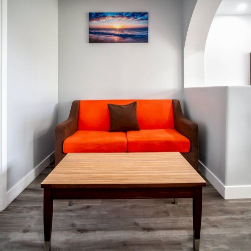 A small living area with an orange couch, a wooden coffee table, and a framed landscape picture on the wall.