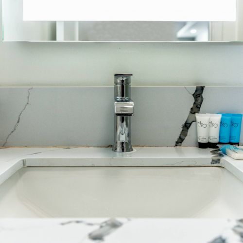 The image shows a marble bathroom sink with a modern faucet and three small toiletry bottles placed on the countertop.