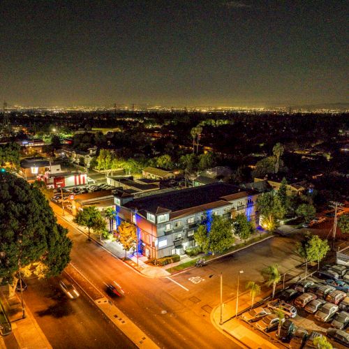 A nighttime aerial view of a city street, showing buildings, streets, and cars, with city lights illuminating the background.