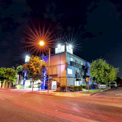 A nighttime street view with a lit building and trees under bright streetlights, featuring empty roads and a visible stop sign.