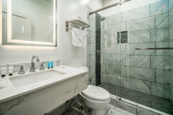 A modern bathroom with a marble vanity, toiletries, a wall-mounted towel rack, and a glass-enclosed shower with tiled walls.