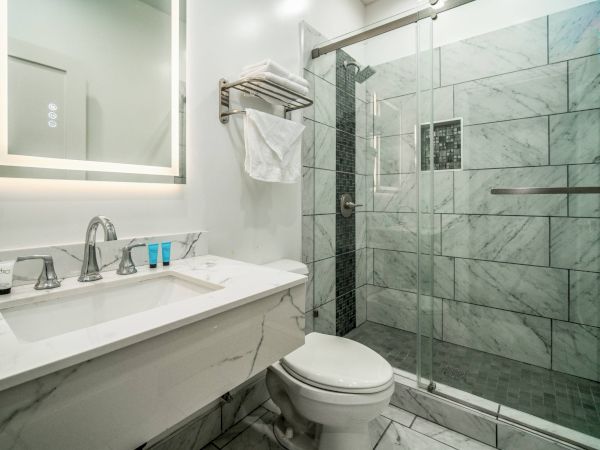 A modern bathroom with a marble vanity, toiletries, a wall-mounted towel rack, and a glass-enclosed shower with tiled walls.