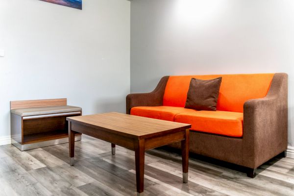 The image shows a room with a brown and orange sofa, a wooden coffee table, a small side table, and a hardwood floor.