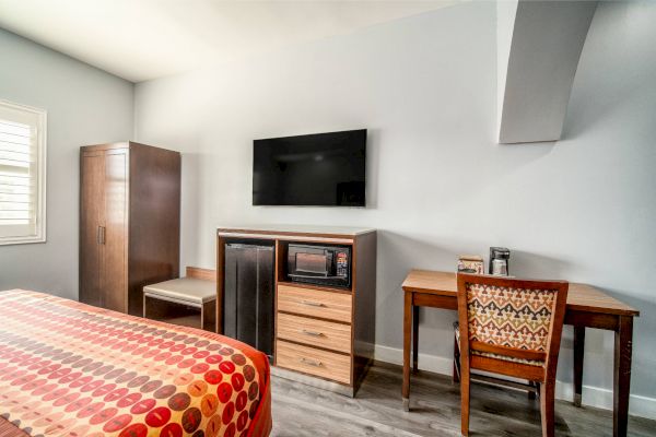 The image shows a room with a bed, wardrobe, desk, chair, TV, fridge, and microwave against a light-colored wall.