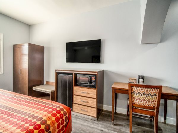 The image shows a room with a bed, wardrobe, desk, chair, TV, fridge, and microwave against a light-colored wall.