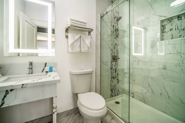 A modern bathroom with a marble sink, toilet, towels, and a glass-enclosed shower with marble walls.