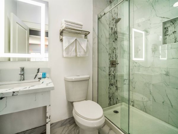 A modern bathroom with a marble sink, toilet, towels, and a glass-enclosed shower with marble walls.