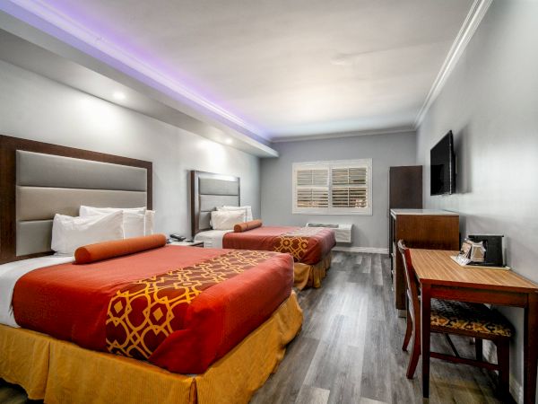 The image shows a hotel room with two double beds, a desk, a TV on the wall, and stylish decor.