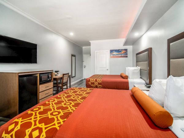 The image shows a hotel room with two beds, a flat-screen TV, a dresser, and a small table with chairs.