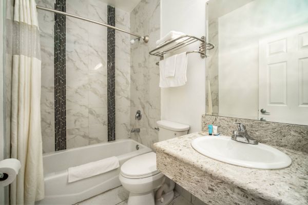 A modern bathroom with marble tiles, a tub with a shower curtain, a toilet, sink, and a mirror. Towels are neatly placed on a rack.