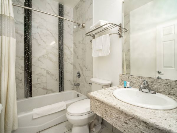 A modern bathroom with marble tiles, a tub with a shower curtain, a toilet, sink, and a mirror. Towels are neatly placed on a rack.