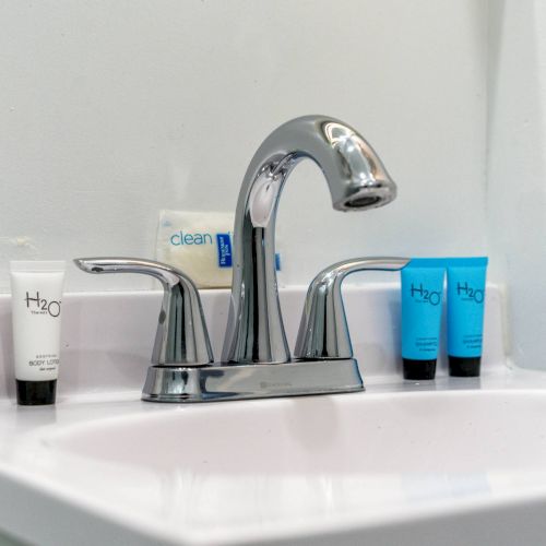 A bathroom sink with a chrome faucet is shown, surrounded by small toiletry bottles and soap on the counter.