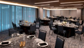 An elegant banquet hall with round tables set for a formal event, featuring black chairs, floral centerpieces, and mood lighting in the ceiling.