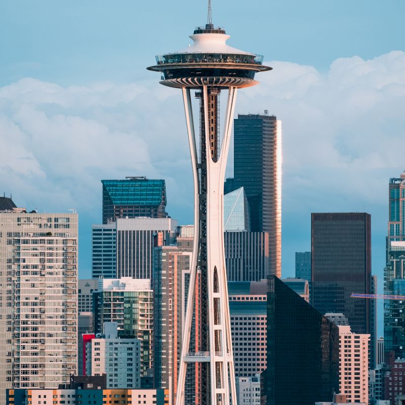The image shows the Space Needle in Seattle, surrounded by tall buildings and a cloudy sky in the background ending the sentence.