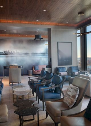 A modern lounge with numerous chairs, large windows showcasing a scenic view of a waterfront and a Ferris wheel outside, and a mural on the wall.