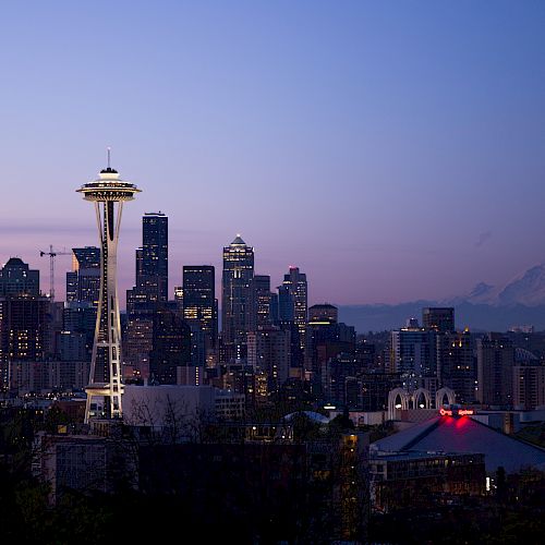 The image shows the Seattle skyline at dusk with the Space Needle prominently featured and Mount Rainier in the background.