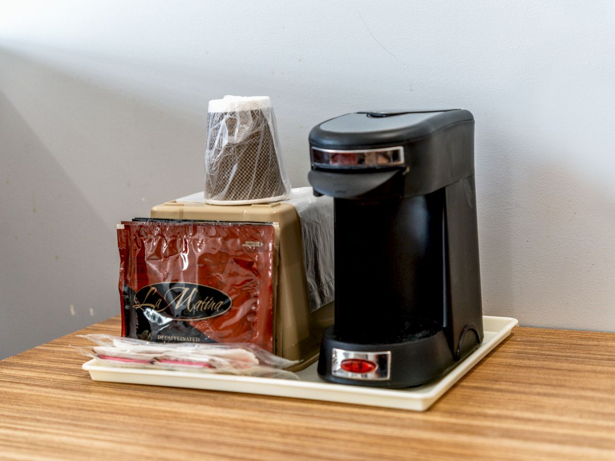 A compact coffee maker setup with paper cups, coffee packets, and stirrers is neatly arranged on a tray on a wooden surface.