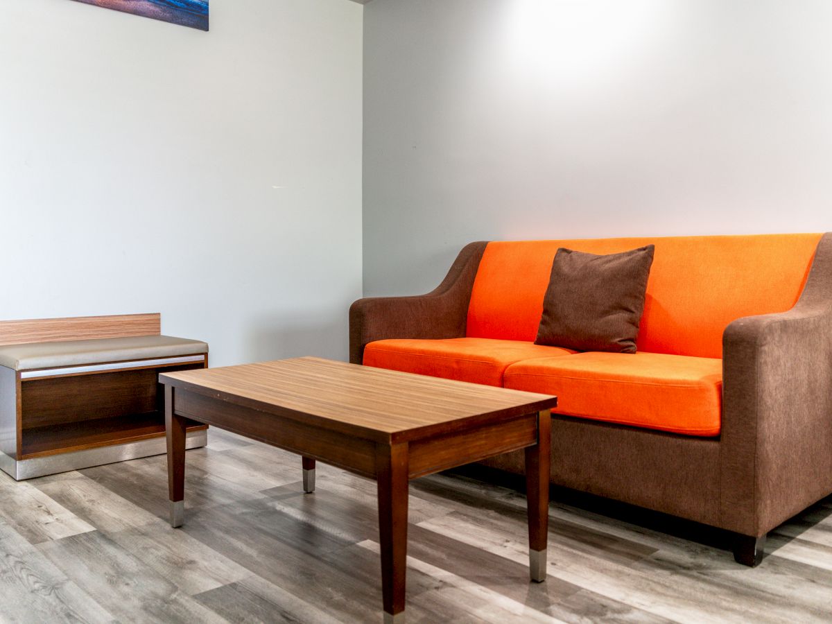 The image shows a small living room with a brown and orange sofa, a wooden coffee table, a side table, and a light-colored floor.