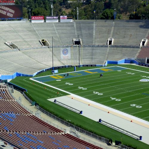 The image shows an empty football stadium with a well-maintained field. There are advertisements visible in the background.