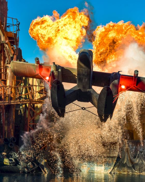 A dramatic scene of a seaplane taking off amidst a large explosion and water splash in an industrial setting, displaying intense action.